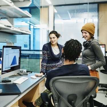 Smiling scientists discussing data on computer while working in research lab